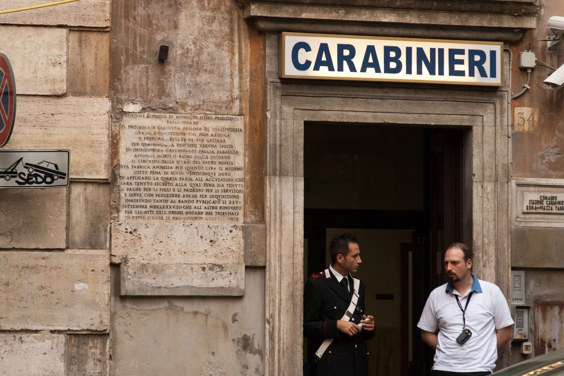 A police station in Rome, Italy, with a uniformed policeman in the doorway, talking to a man with a walkie-talkie.