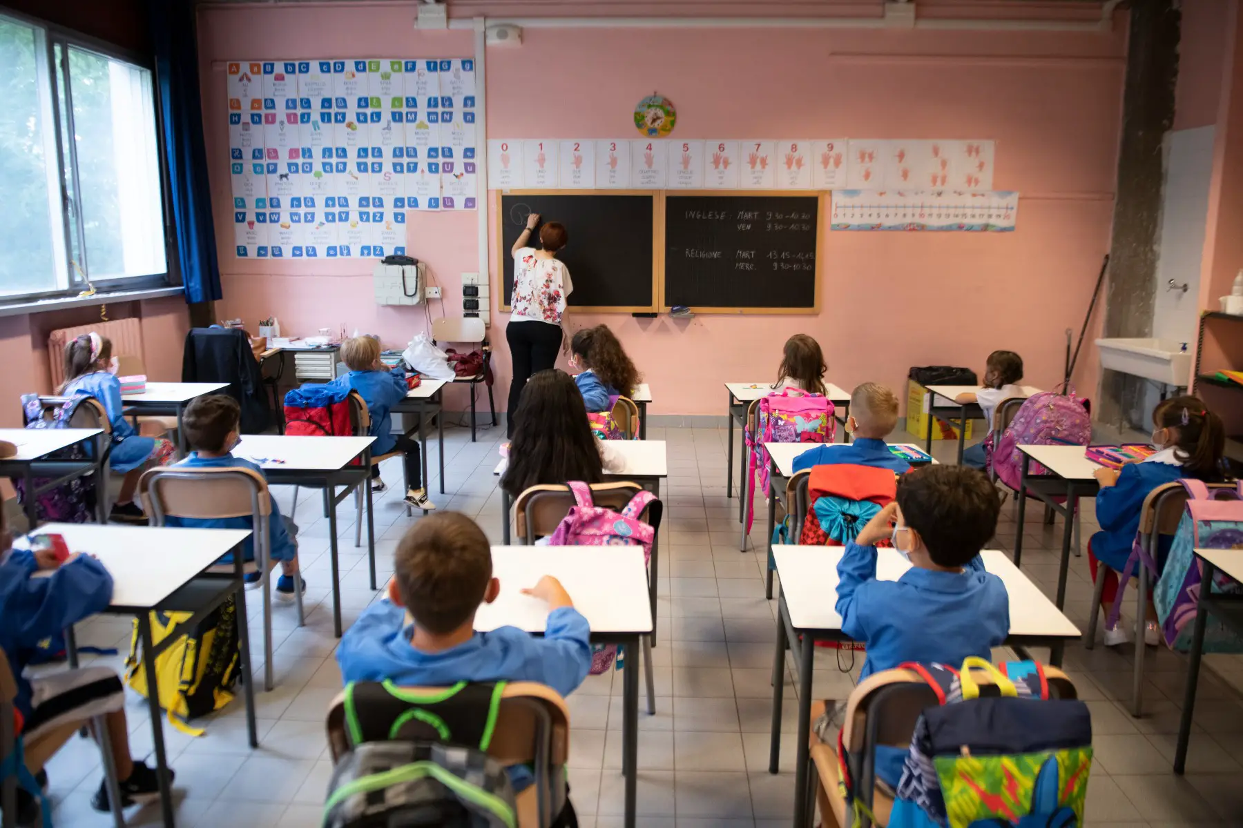 Children wearing protective masks inside an elementary school classroom with separate desks in Torino, Italy. 
