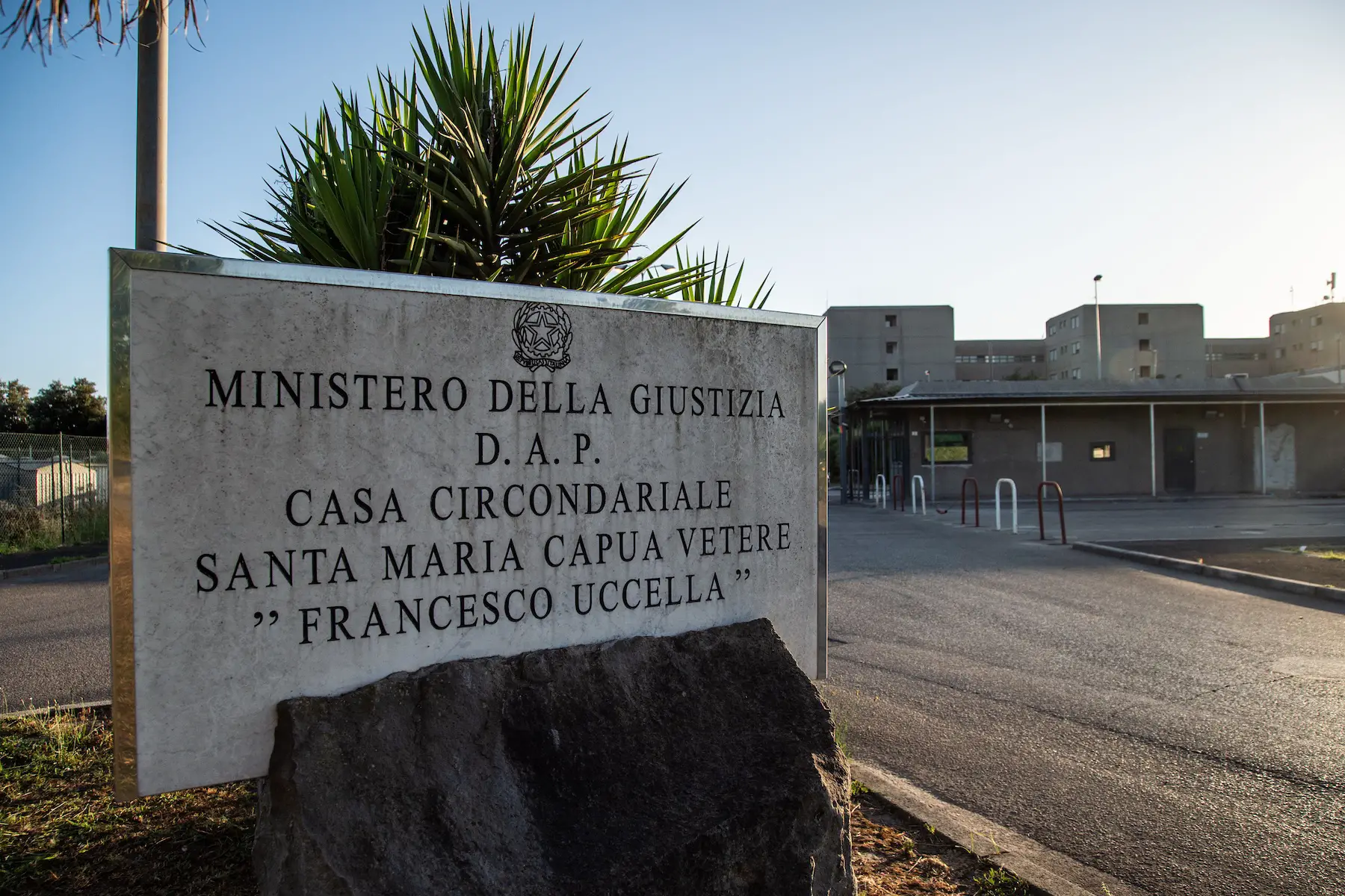A large stone Ministry of Justice sign stands mounted on a rock in front of the Santa Maria Capua Vetere prison