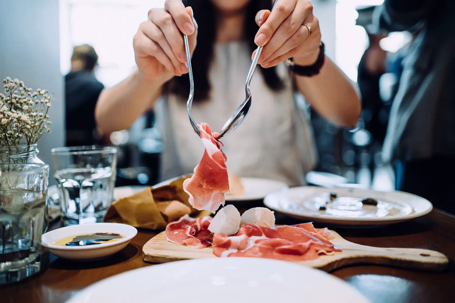 A close up and midsection of woman taking a piece of prosciutto off a plate of antipasti