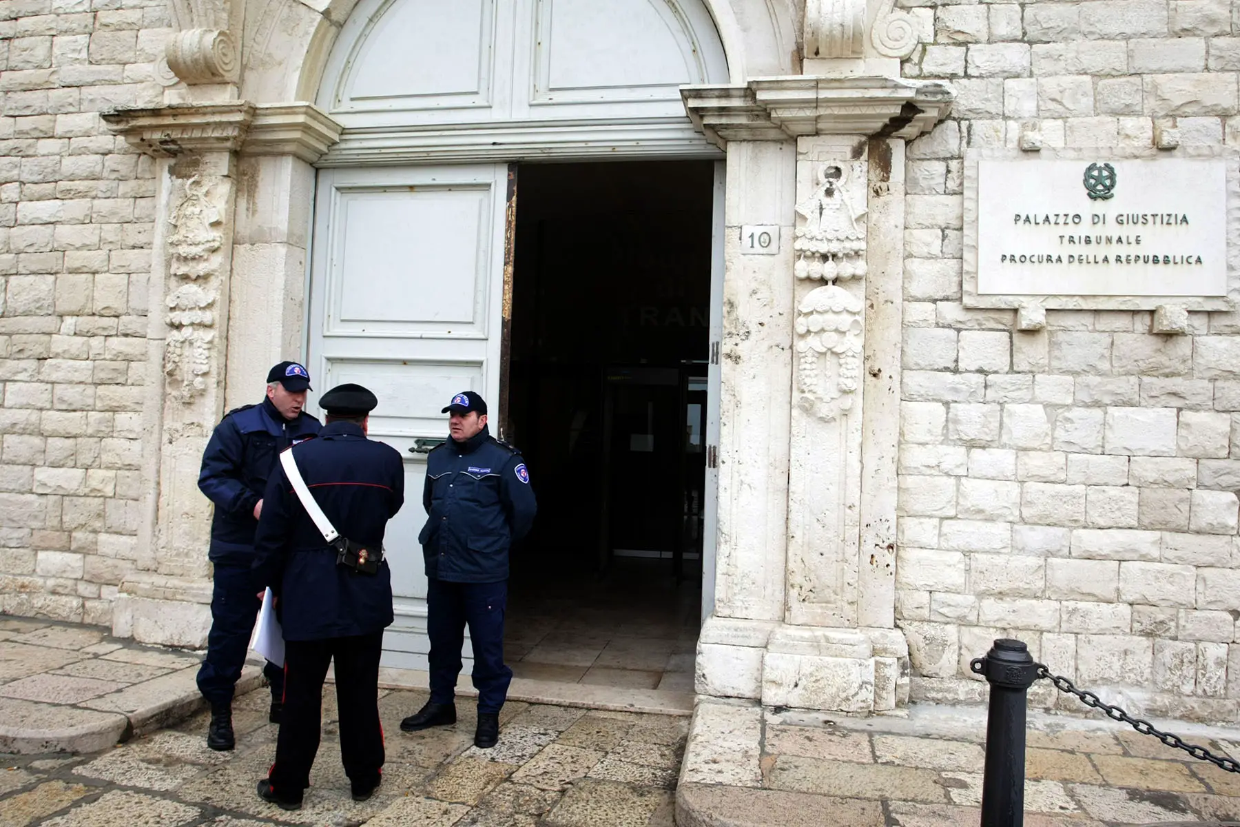 Three law enforcement officials standing outside public prosecutor's office in Trani, Italy. 