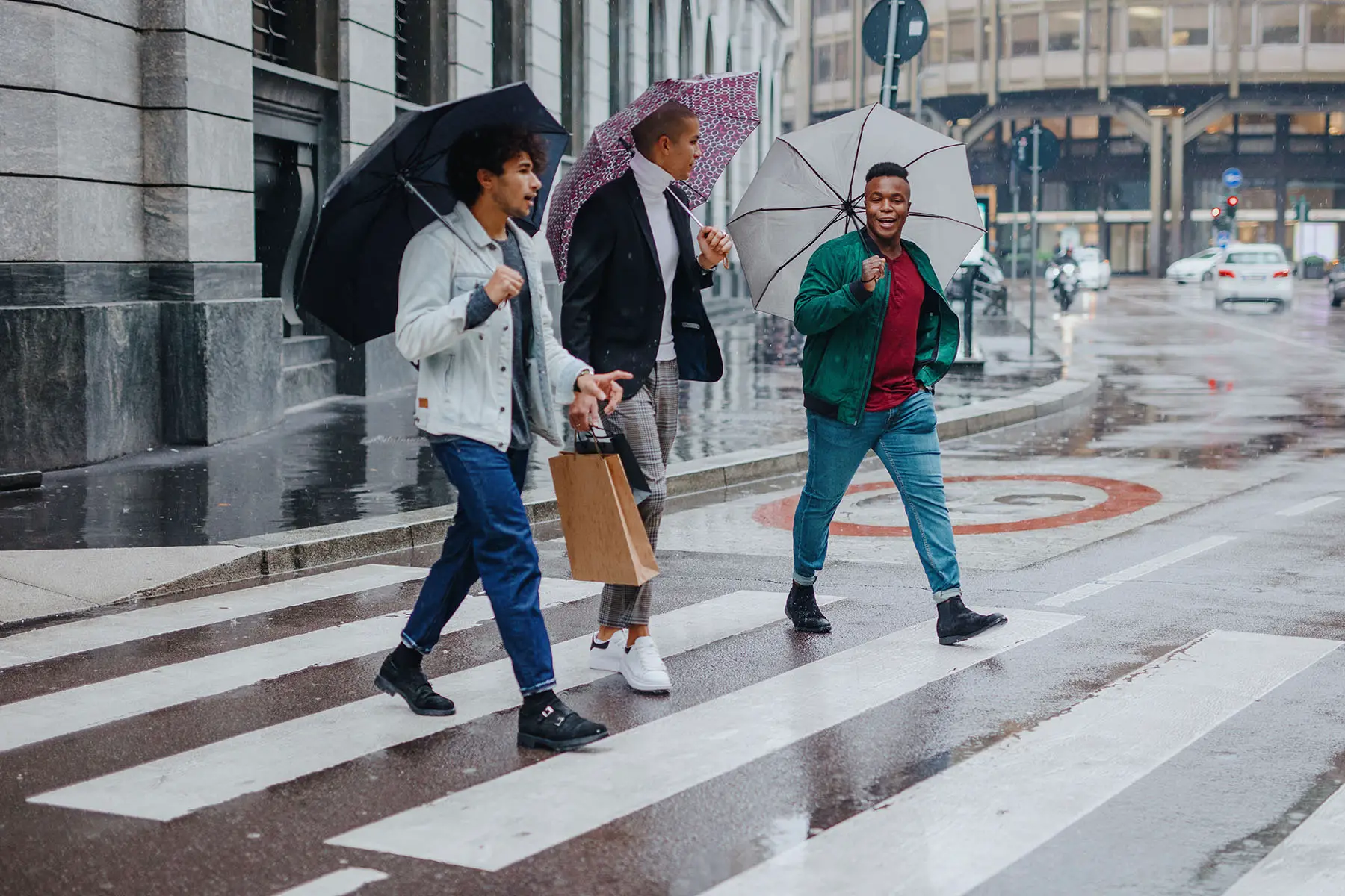 Three young men with shopping bags walking in the rain holding umbrellas.