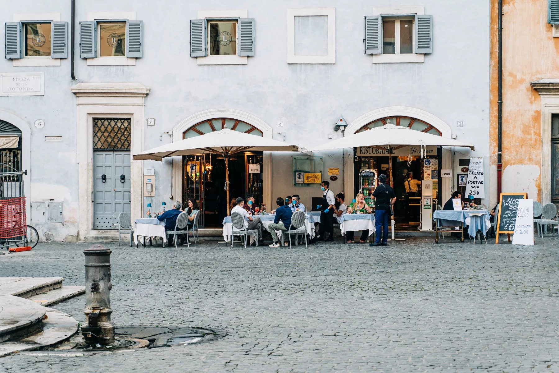 People sit at outdoor tables on a stone-paved courtyard at an Italian restaurant in Rome.