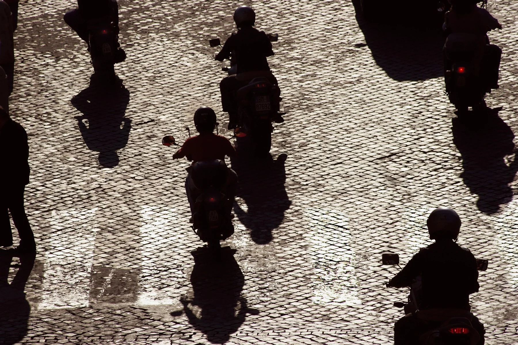 Sunlit silhouette view of commuters on scooters in Rome, Italy.