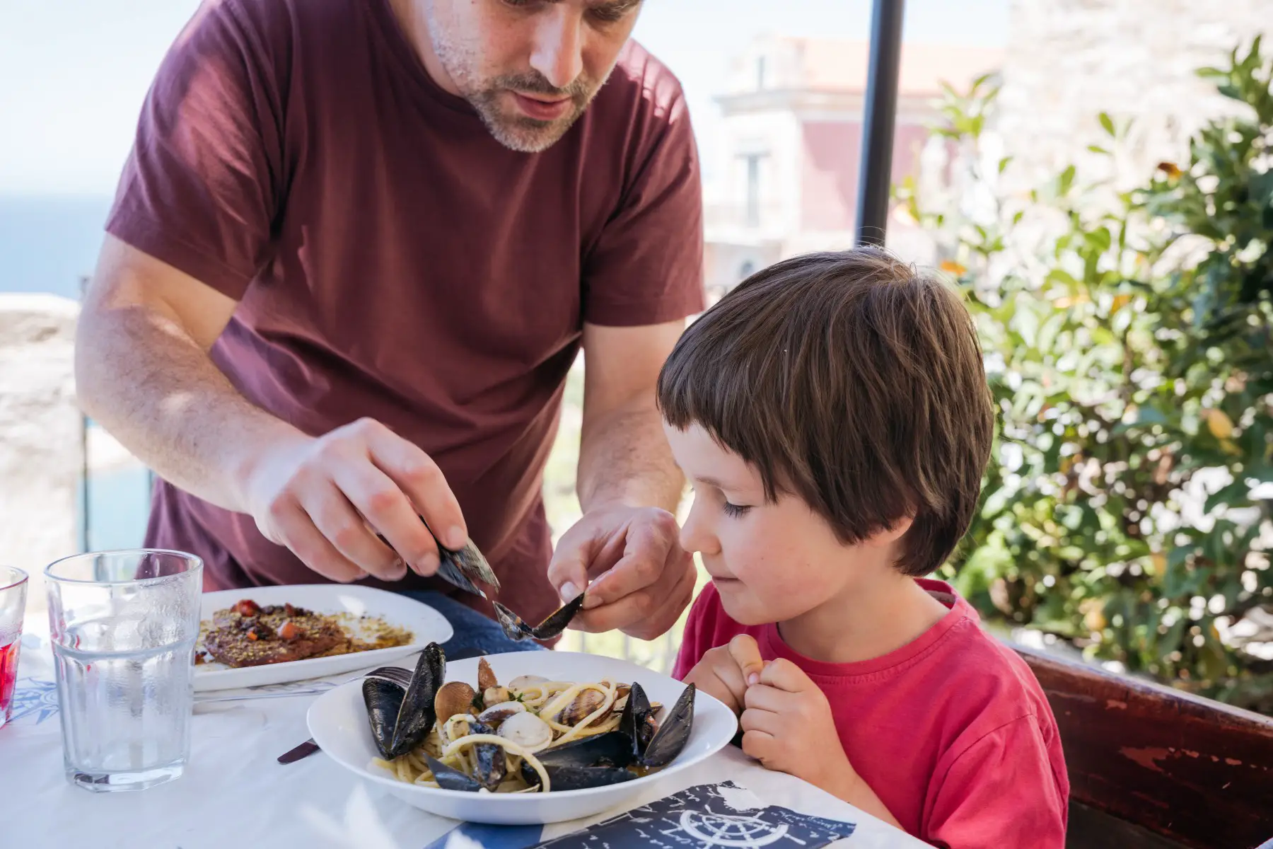 A father showing his young son how to eat mussels on the terrace of a restaurant in Agropoli, Italy