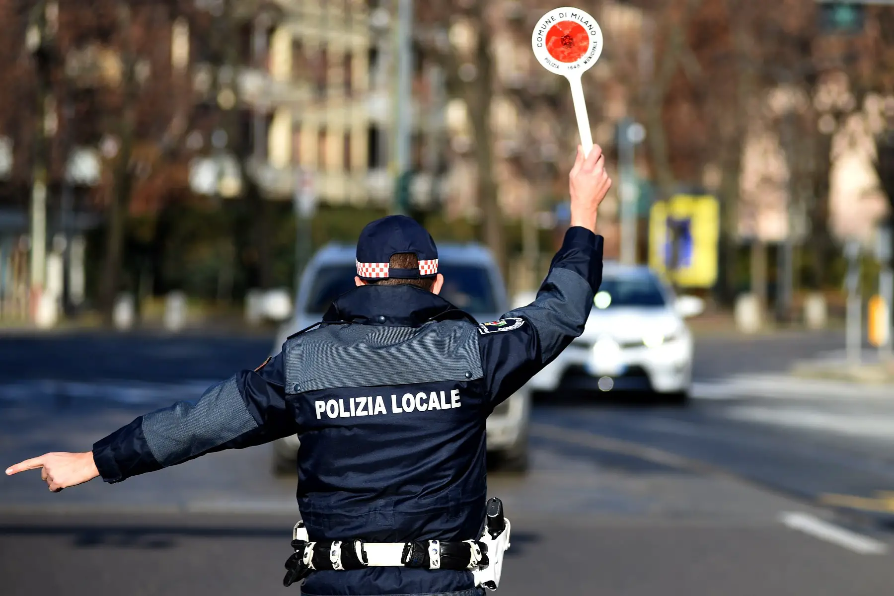 A local police officer in Milan, Italy, holding a stop sign and directing traffic to the side