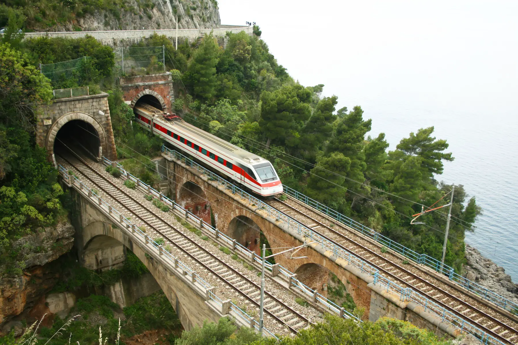 High angle view of a train exiting a mountain tunnel, driving on a bridge in Maratea, Italy.