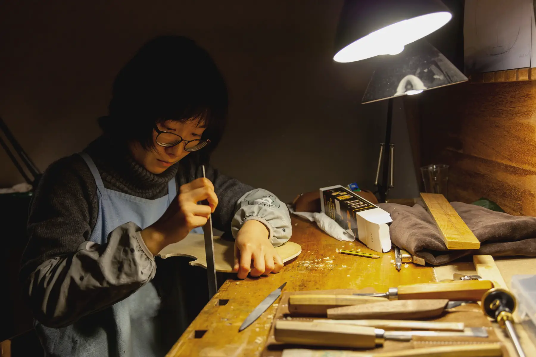 Craftsperson at a work bench concentrating on sanding the back of a violin.
