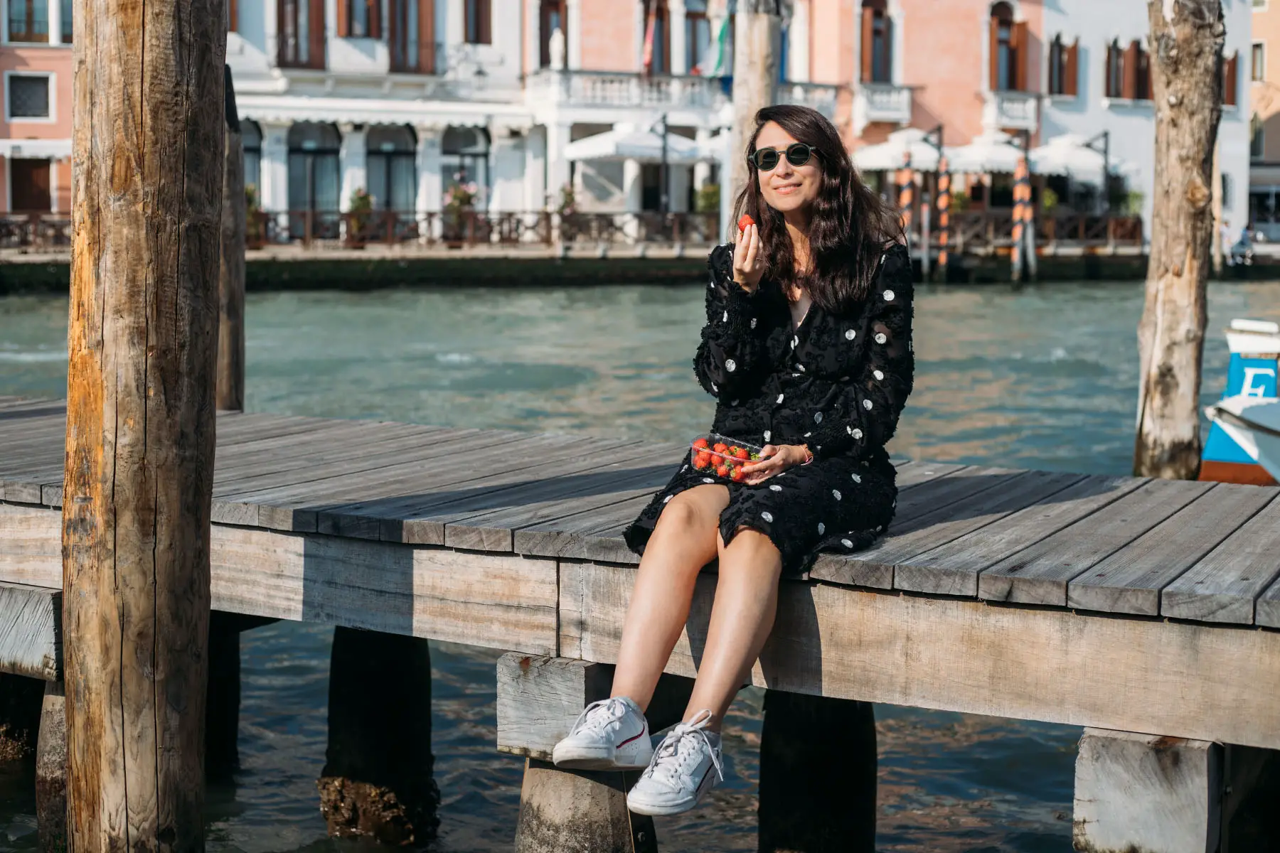 Woman in black sitting on the docks and eating strawberries in Venice, Italy.