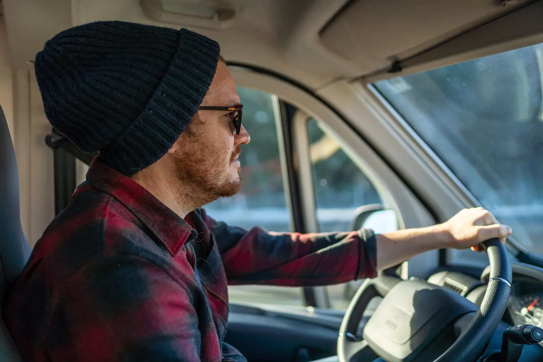 A hipster man with a beard, sunglasses, and beanie hat driving a van