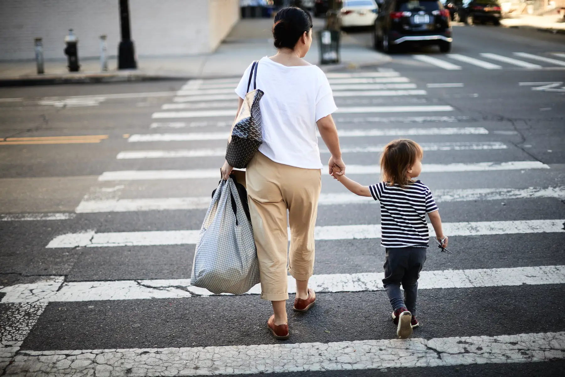 A mother carrying heavy bags while crossing the street with her young child in a busy city