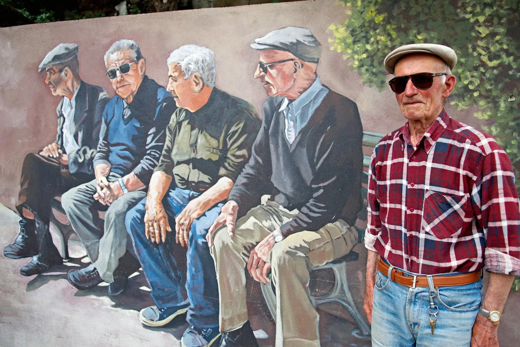 A senior citizen standing next to a mural of pensioners in Tinnura, Sardinia