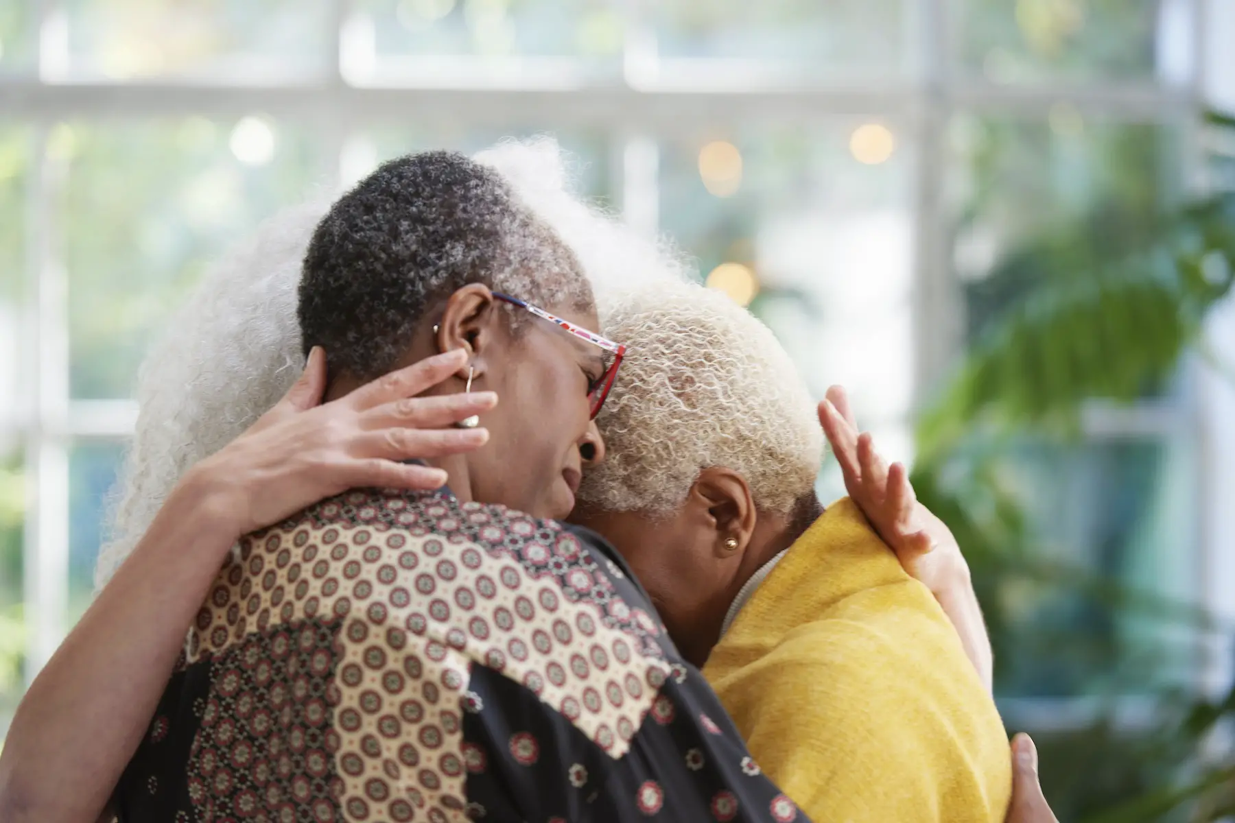 A close-up shot of three older women hugging each other in a brightly lit room