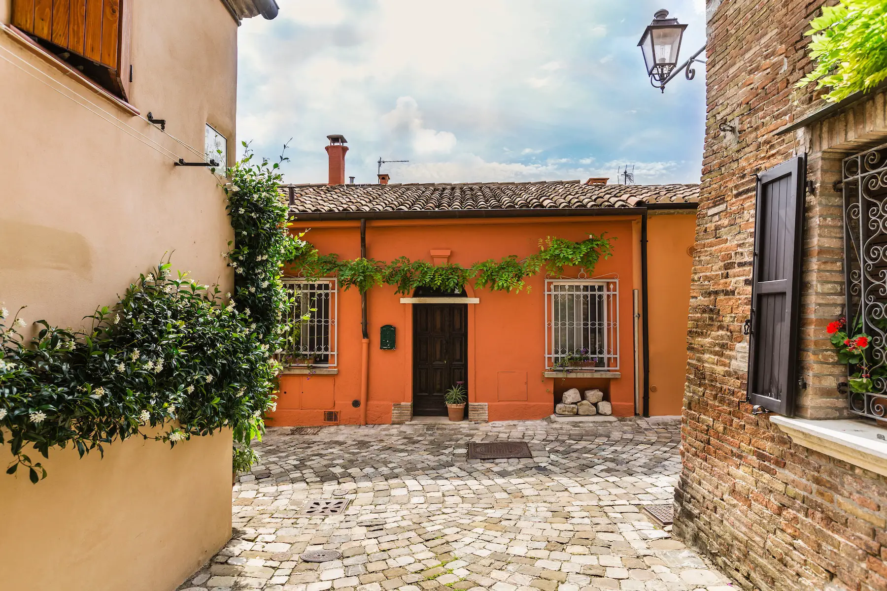 A single-story orange house lies at the end of a quaint, empty alley paved with stones