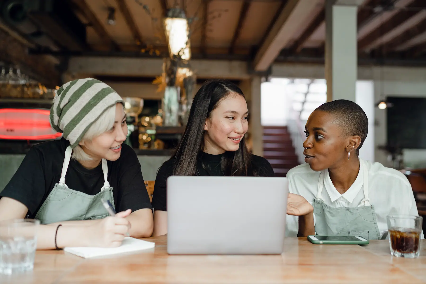 Three female employees of a small business sit chatting at a table inside their cafe