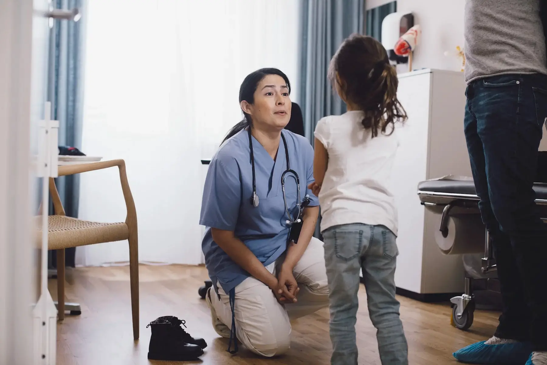 A pediatrician kneels on the clinic floor to speak to a young girl