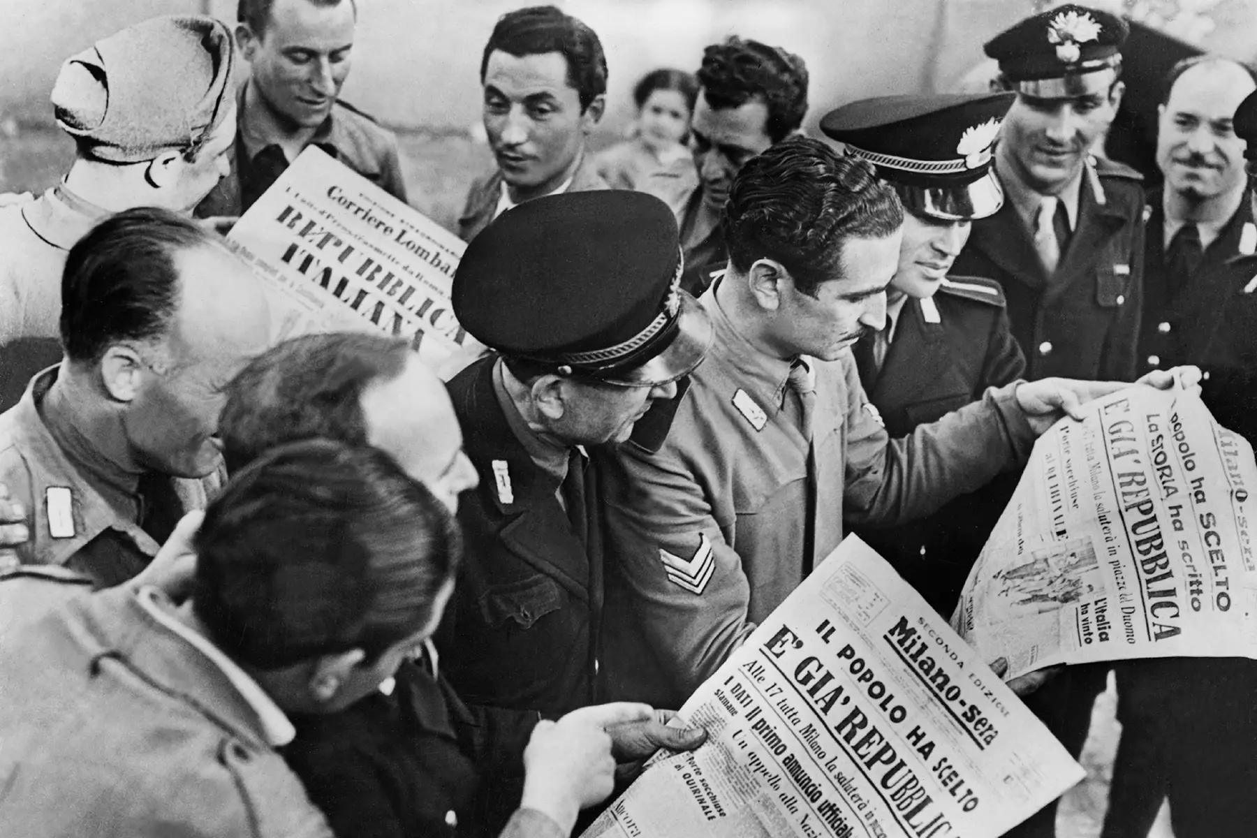A black-and-white photo of a crowd of people reading newspapers with headlines in Italian