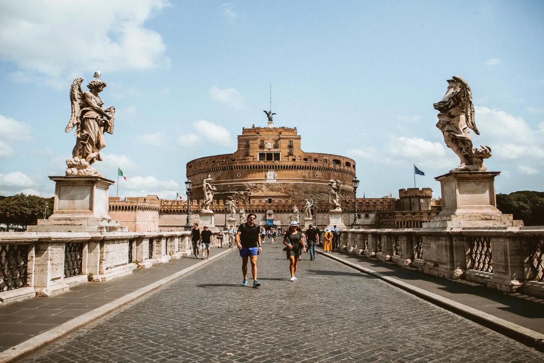 People walking across the Ponte Sant'Angelo in Rome, with the Colosseum in the background