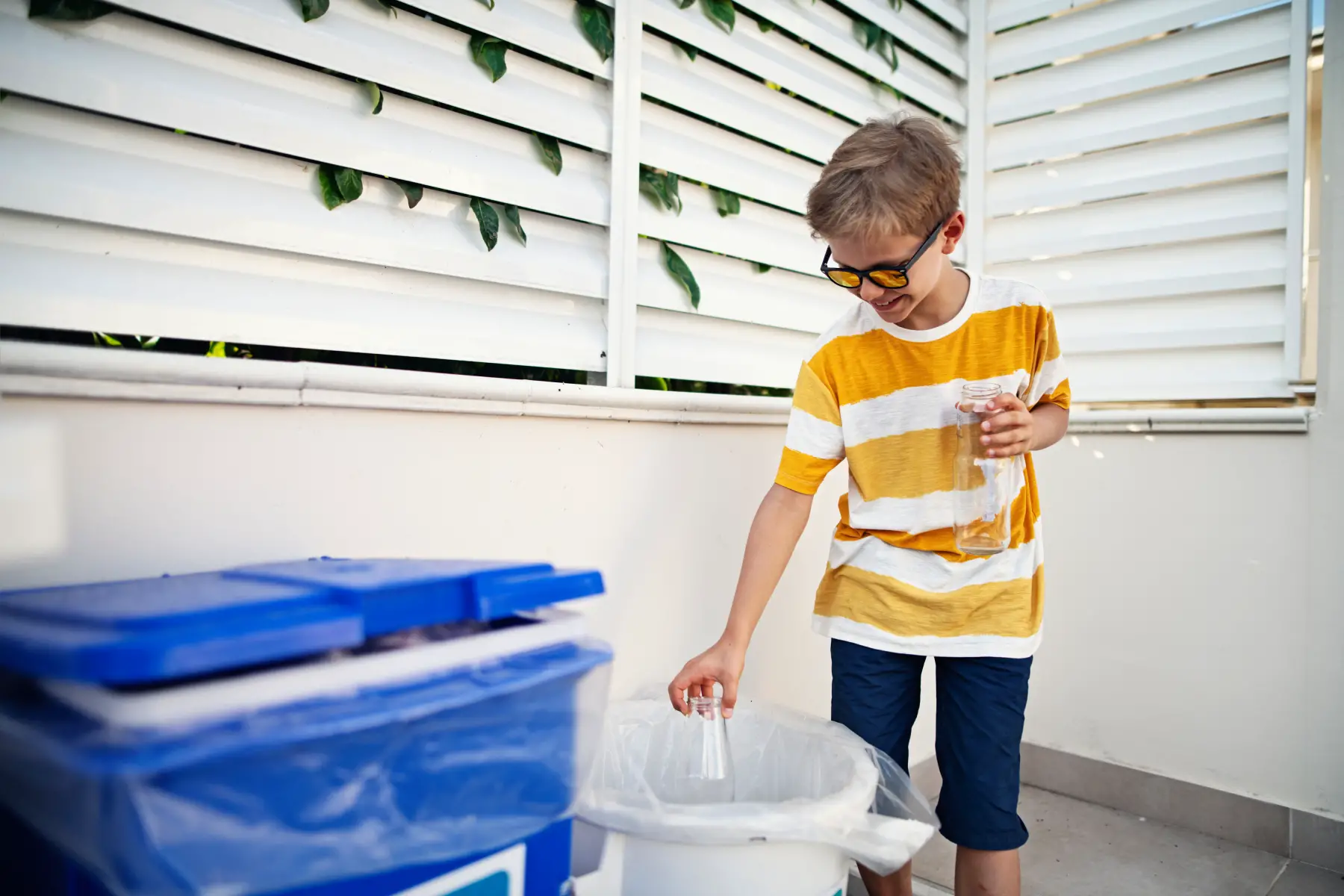 A boy puts a glass bottle in recycling bin