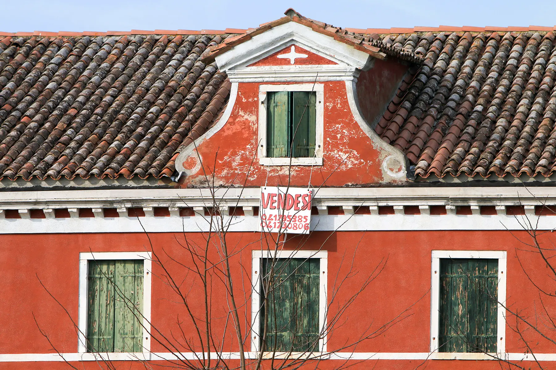 Close-up of a bright red house with a tiled roof, a for sale sign in Italian hanging from the highest window