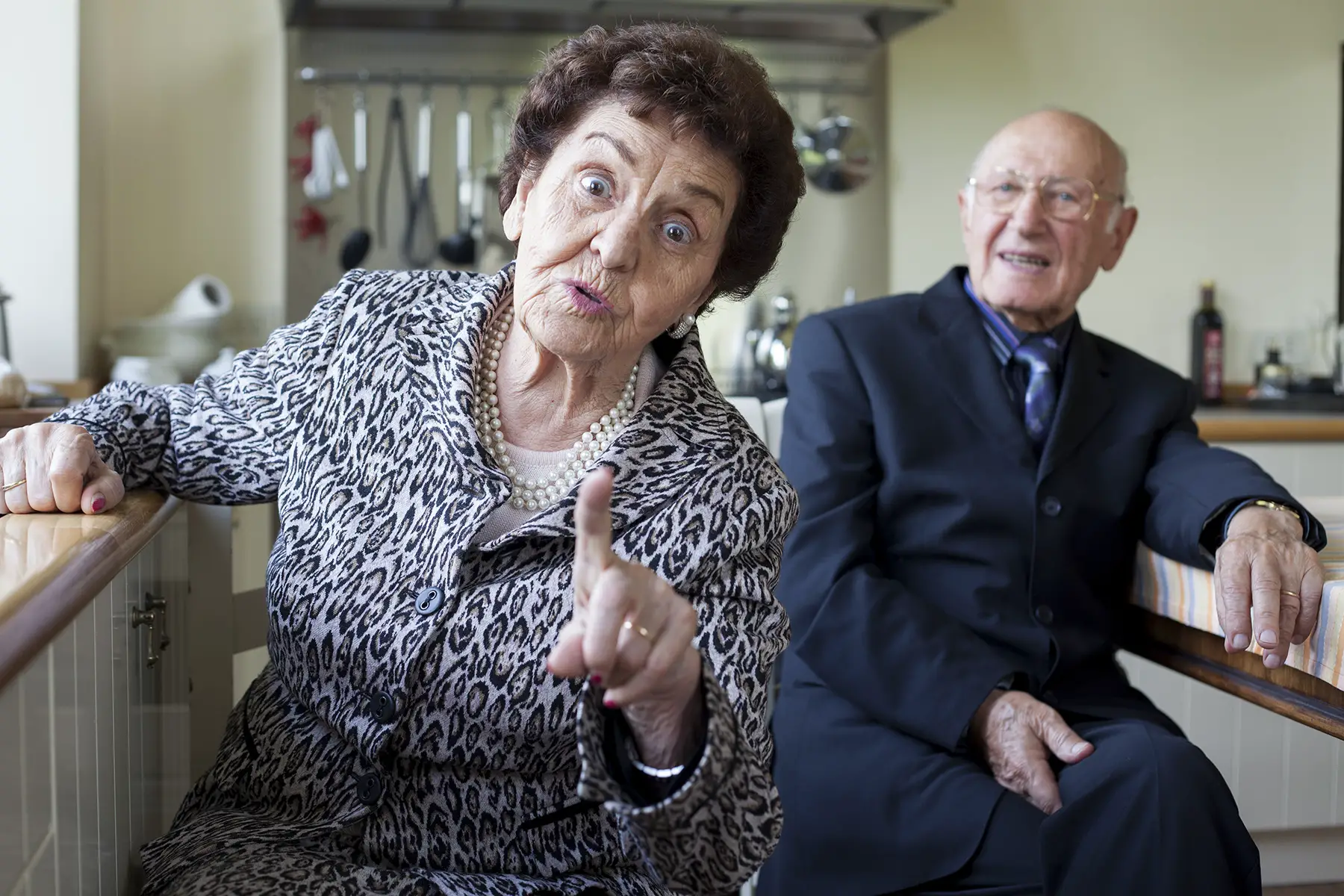 Retired couple in Italy, looks straight at camera, woman holds up her finger as if she is making a point or telling someone off