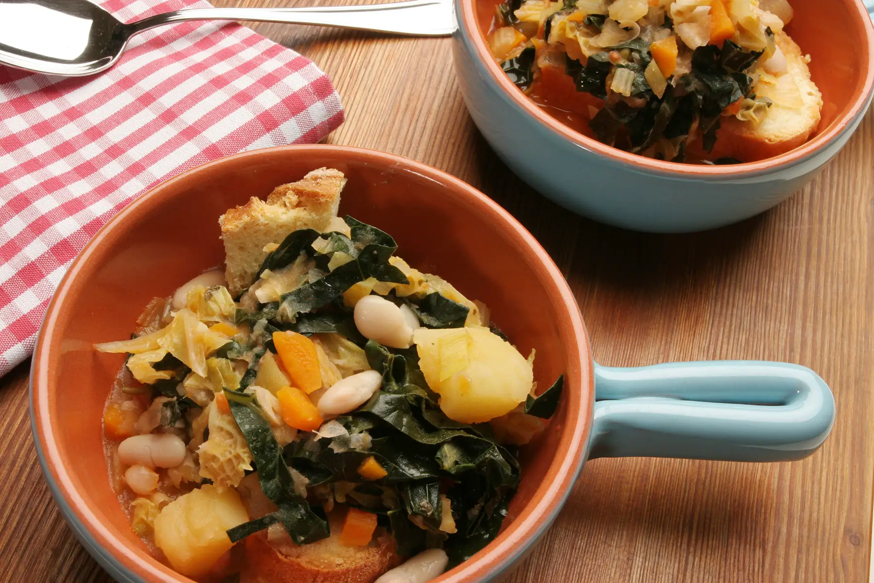 Ribollita – a chunky soup with beans, spinach, and stale bread in a brown bowl with a handle