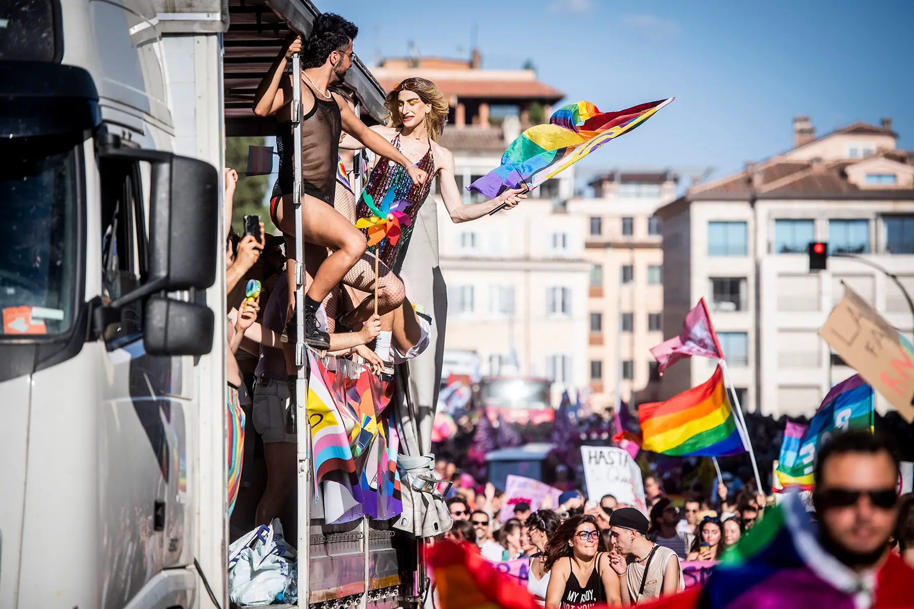 People celebrating with rainbow flags, hanging out of an open truck