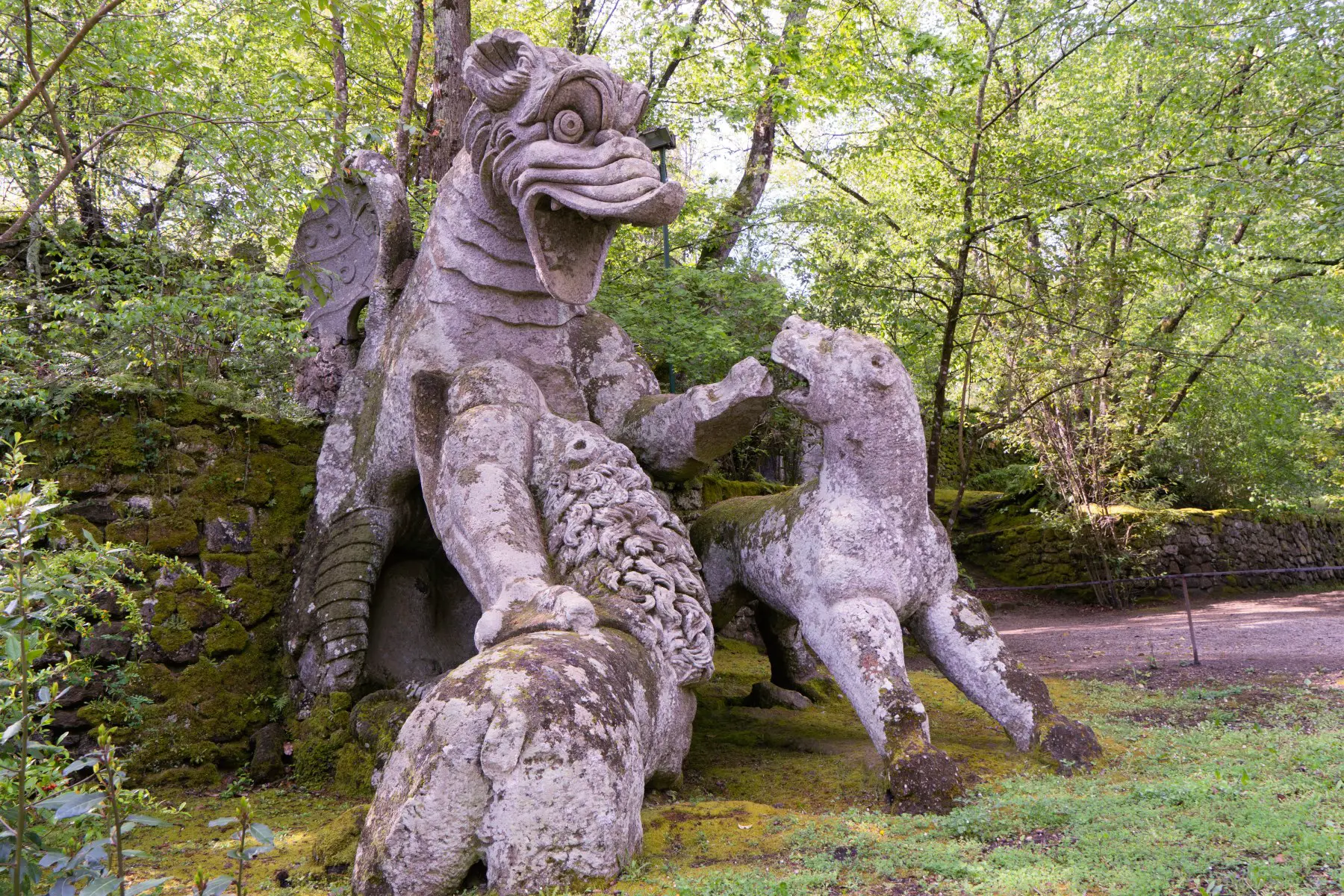 A large stone statue of a dragon in a forest at Sacro Bosco garden in Italy
