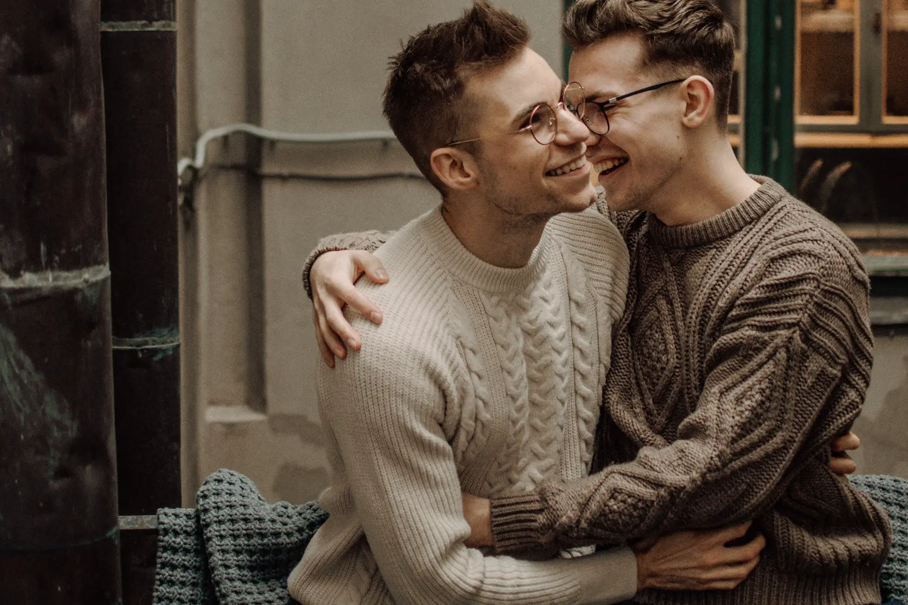 Two men embracing affectionately outside a building with a window