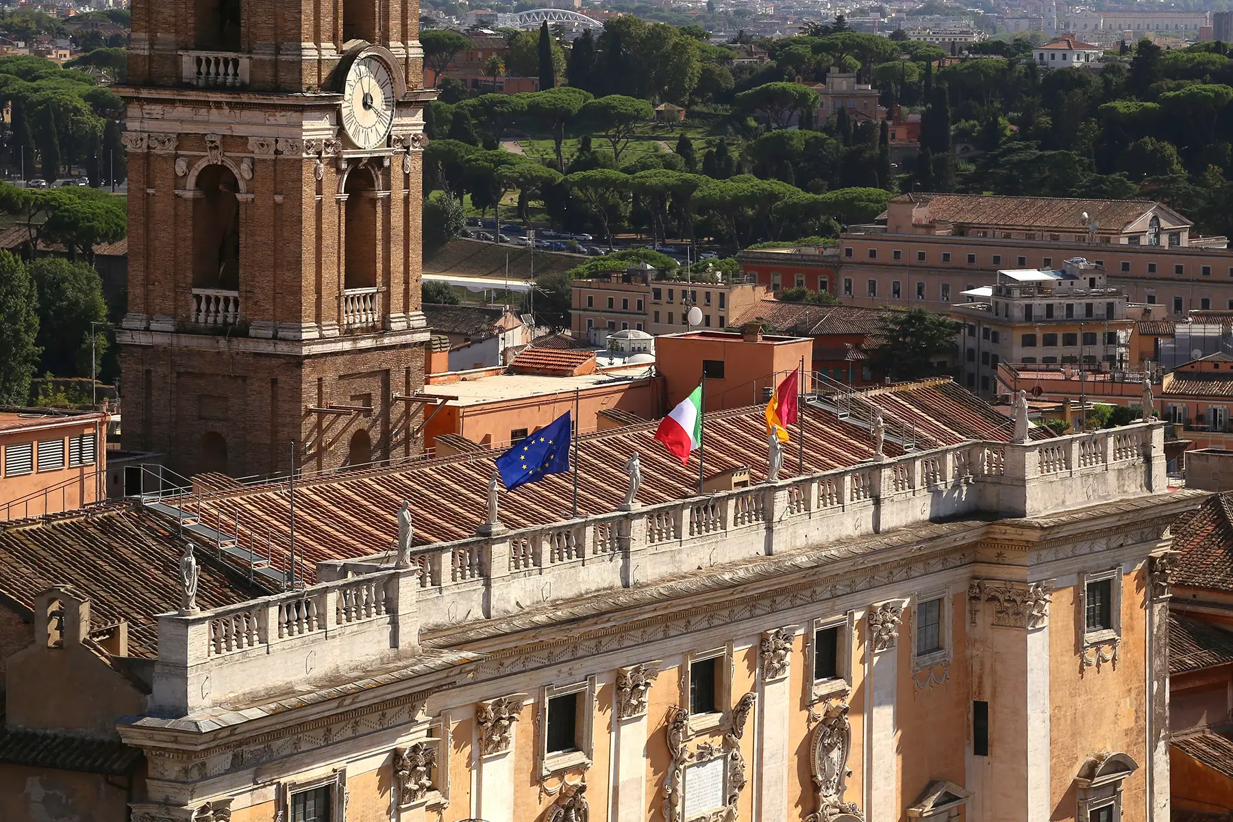 An old-fashioned parliamentary building with an EU flag, an Italian flag, and the flag of Rome (seems to be black, yellow, and red, but not entirely visible)