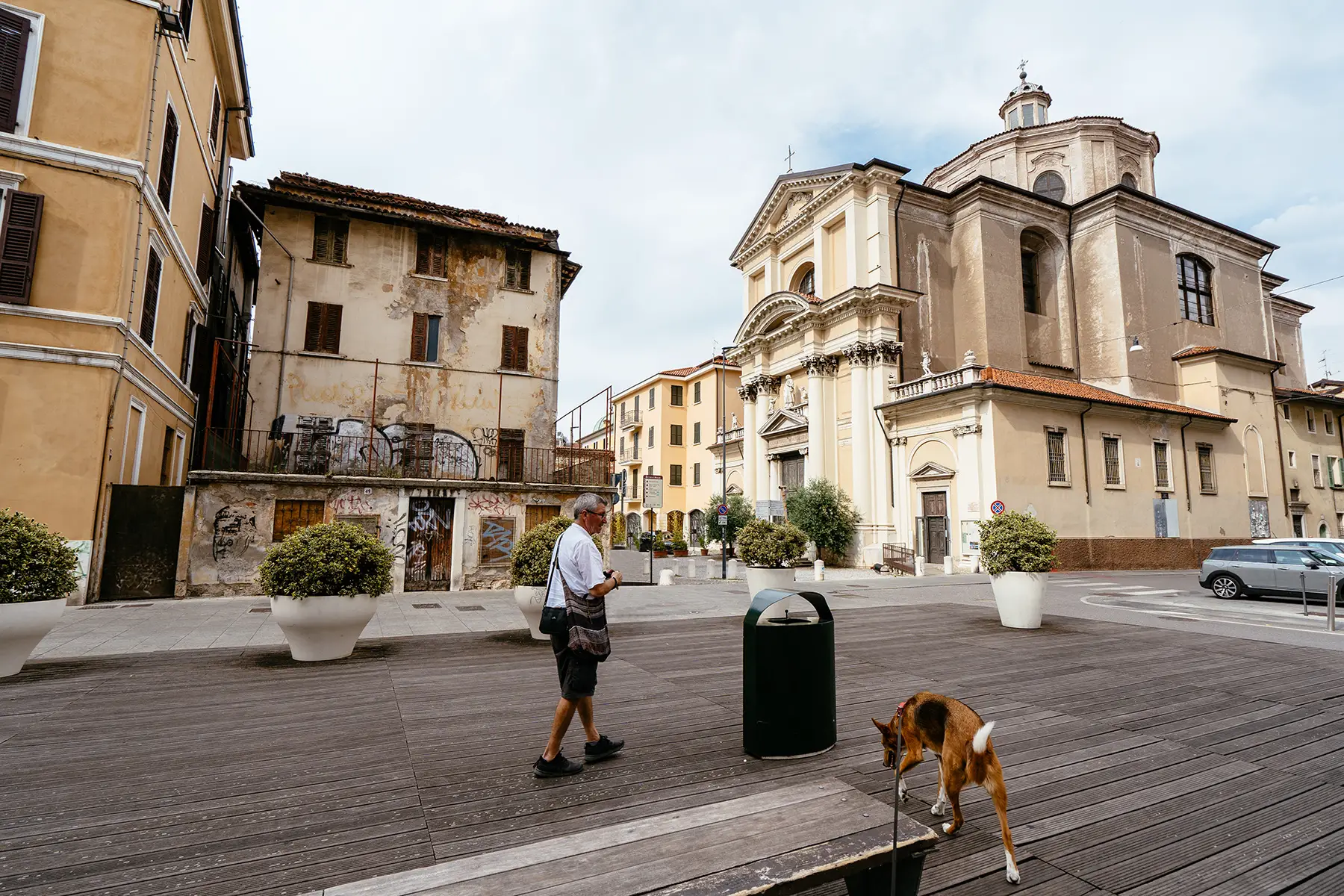 A senior man walking near a dog in front of San Lorenzo Church, an old church in Brescia, Italy