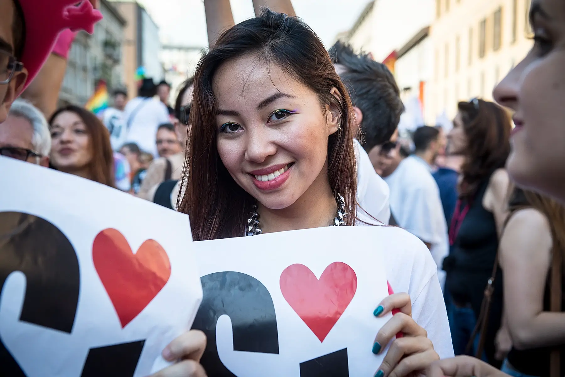 A woman holds up a sign with 'Sí' written on it. The dot of the í is a heart.