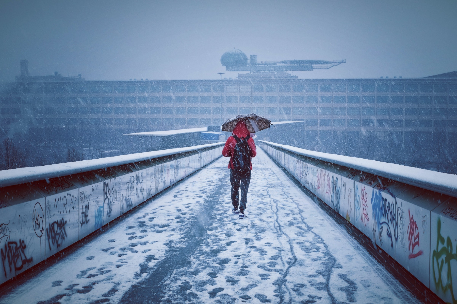 Person walking through snowfall in Turin, with colorful graffiti on both sides of the bridge