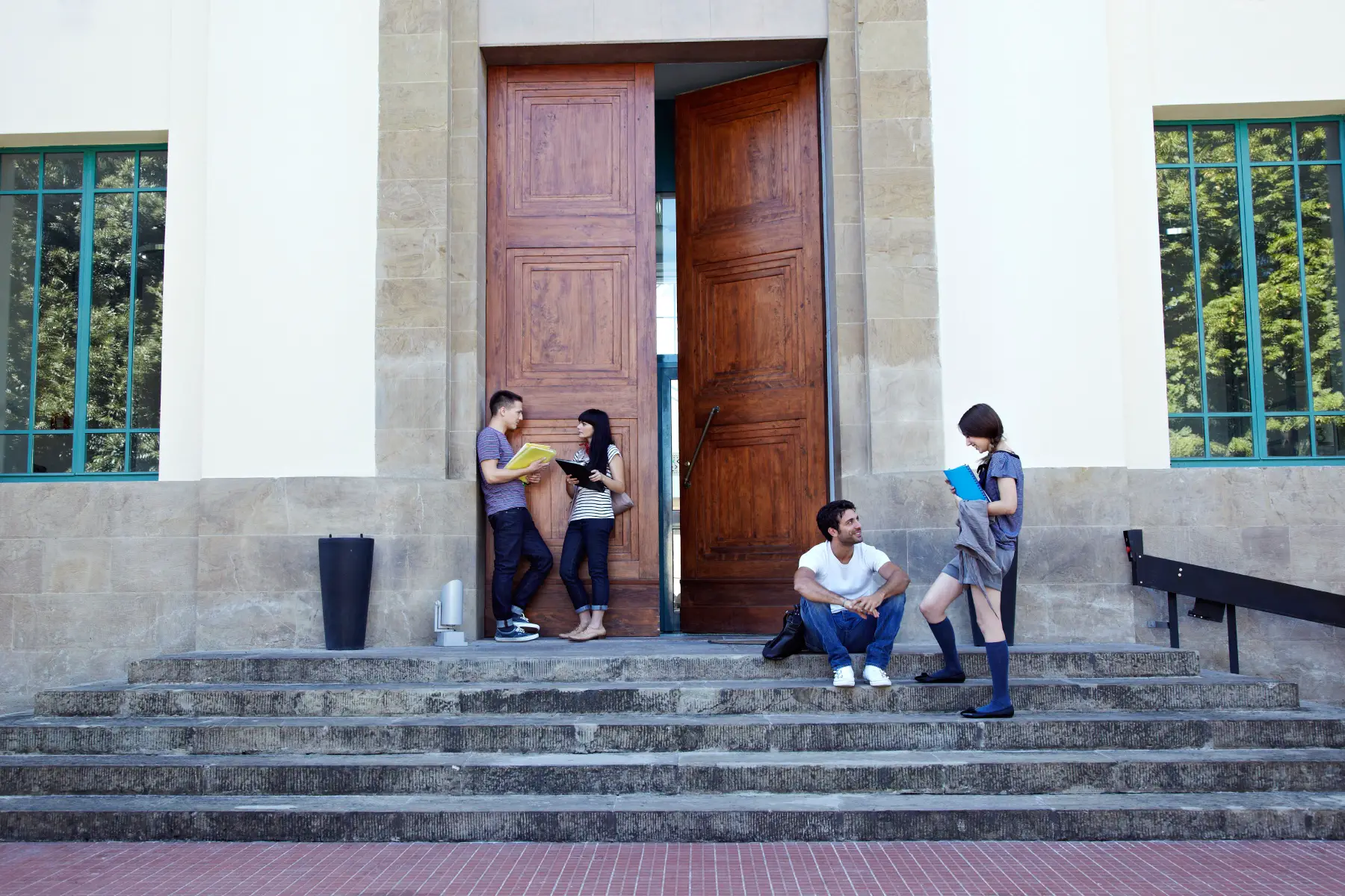 Students chatting on stone steps in front of large wooden doors - possibly at the university