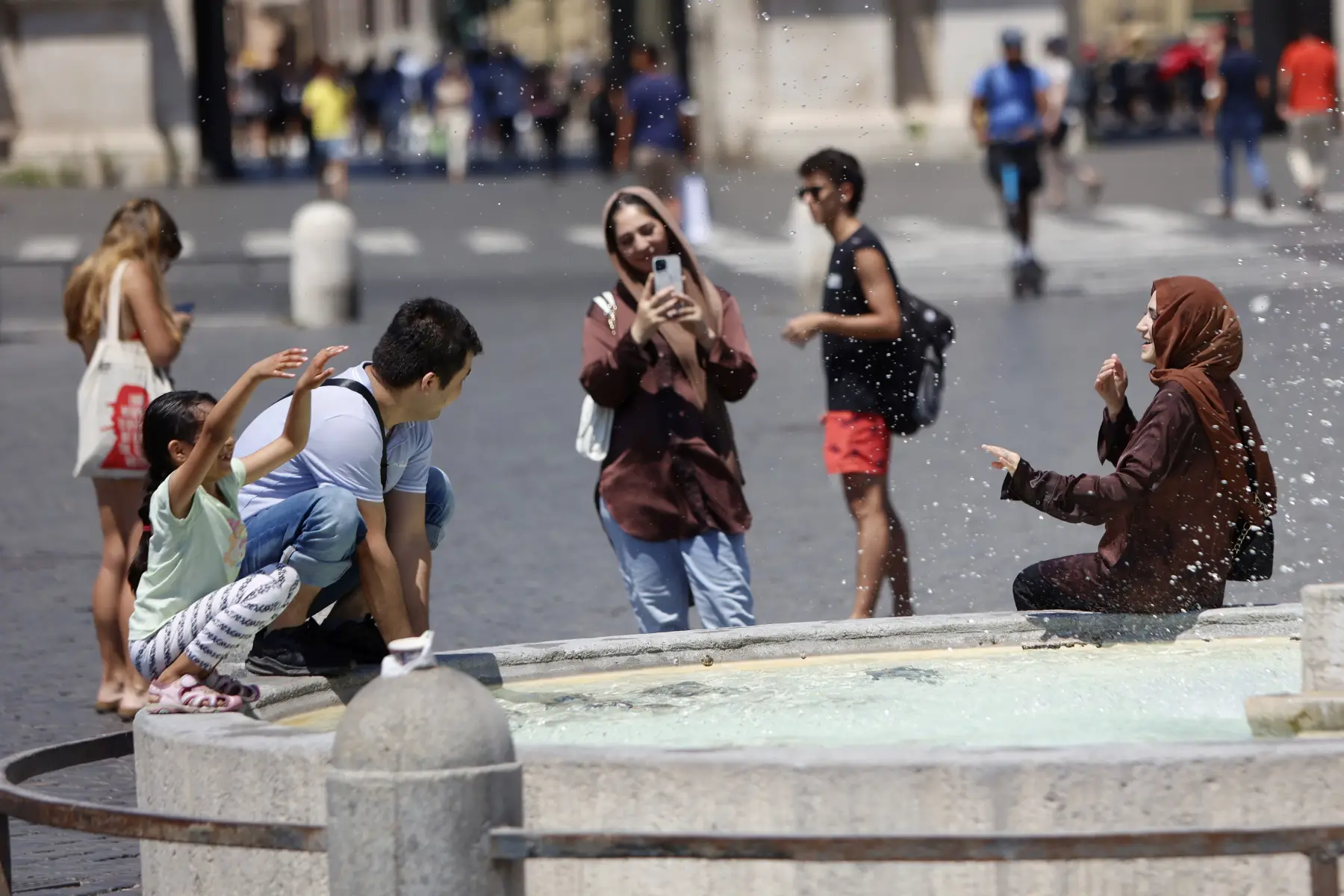People cooling down with water from a fountain on a very hot day in Rome, taking photos.