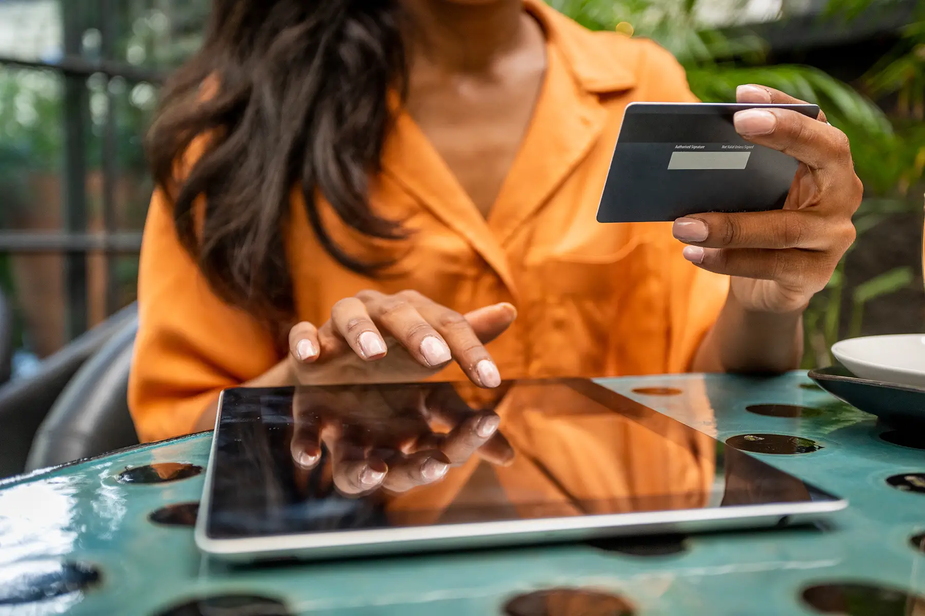 Close-up of a woman using a tablet and holding a credit card