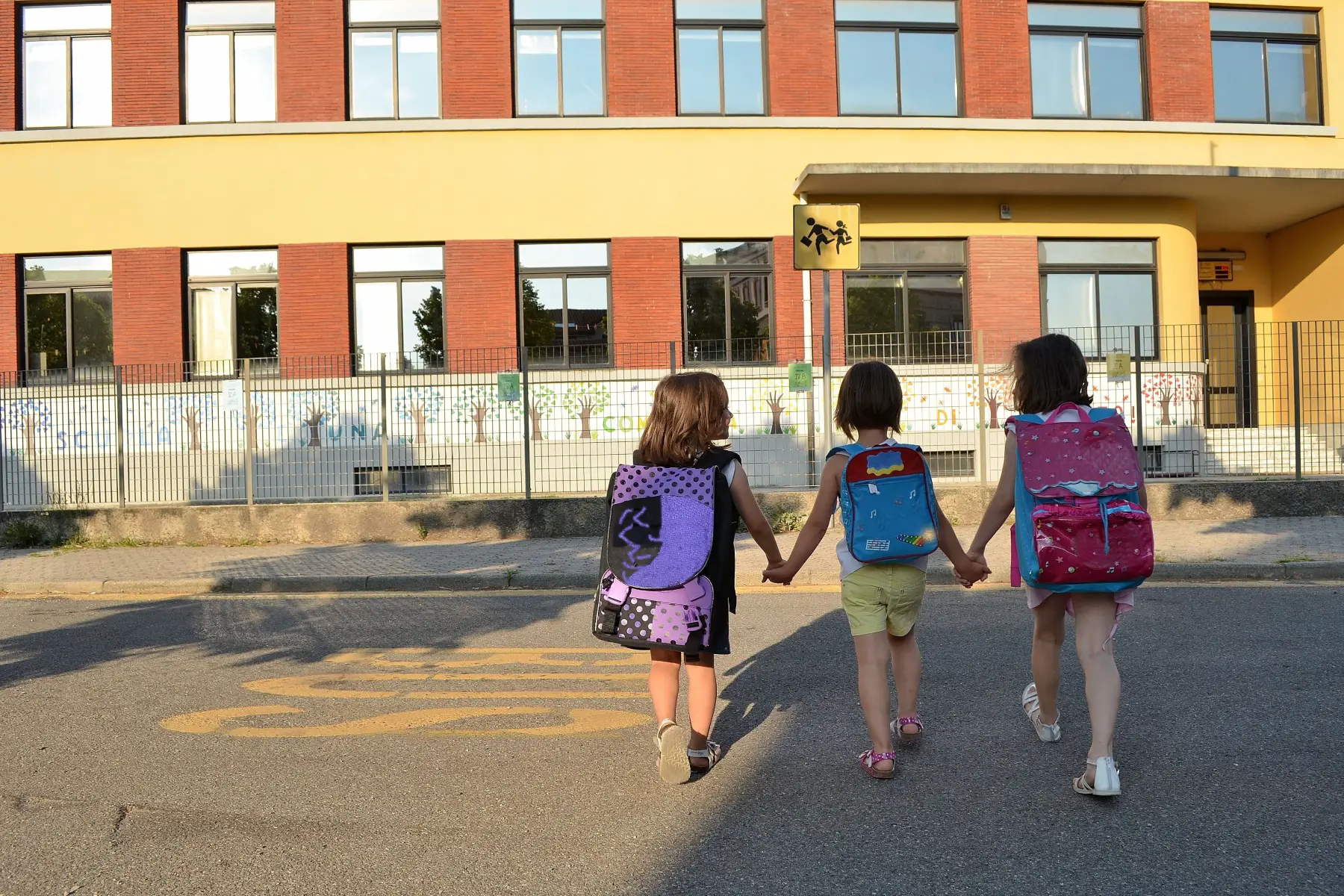 Three friends crossing street to primary school, walking holding hands