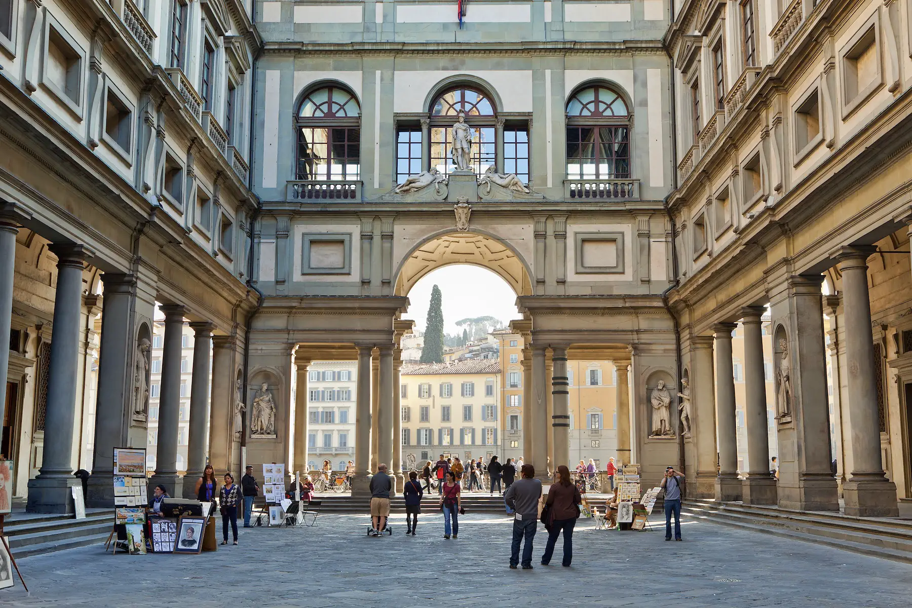 Tourists and art sellers gather in the Vasari Corridor of the Uffizi Gallery, Florence on a sunny day.