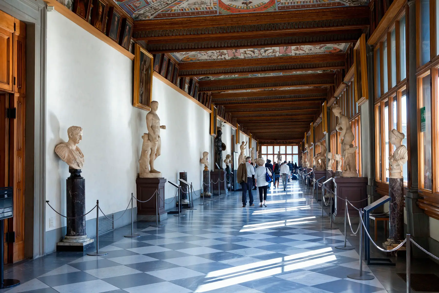 Visitors walking down the sunny halls of the Uffizi Gallery