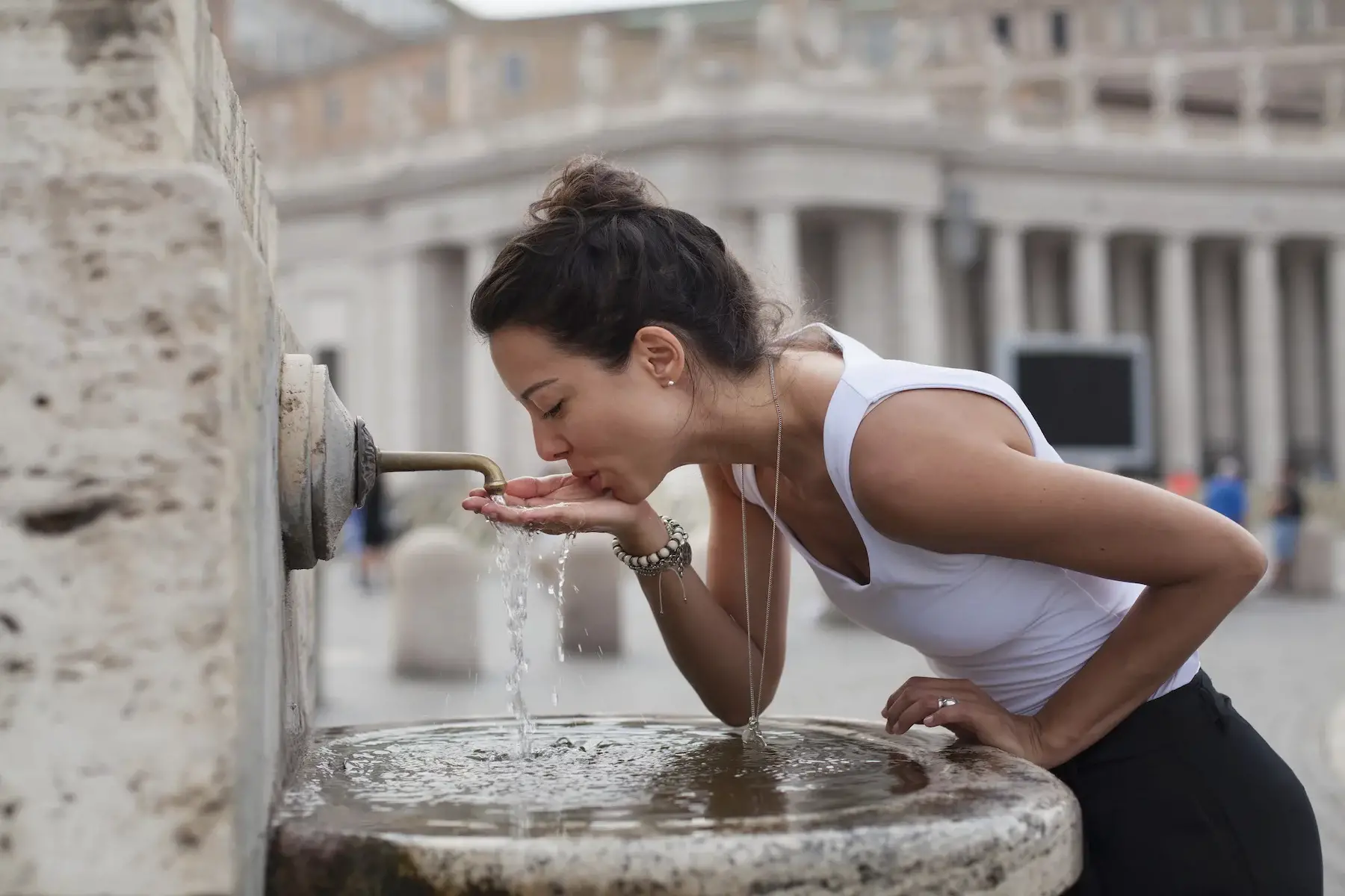 A young woman cups her hand to drink from a water fountain at Saint Peter's Square in Rome