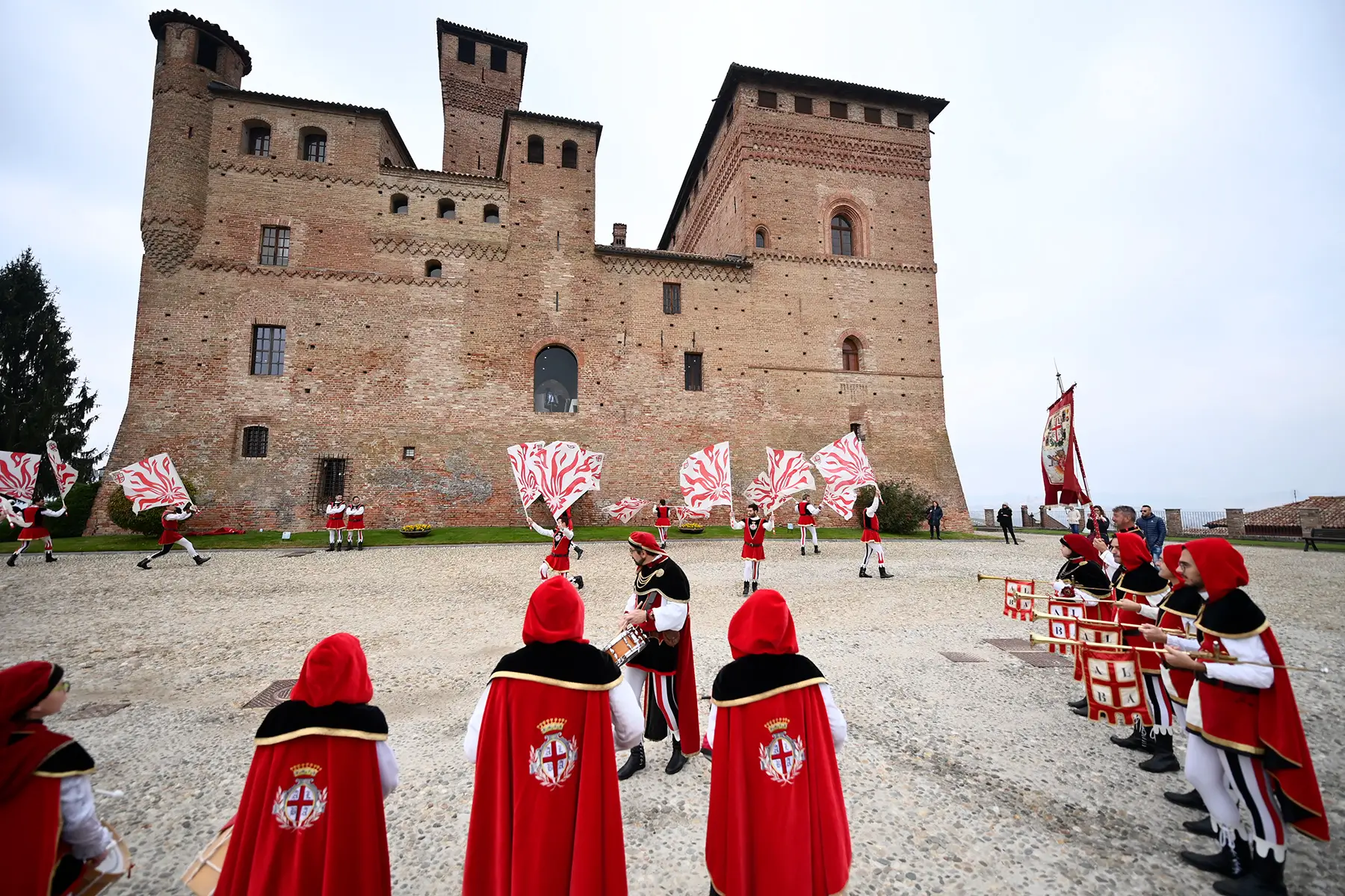 People outside a castle, dressed in red and white medieval costumes, waving white and red material.