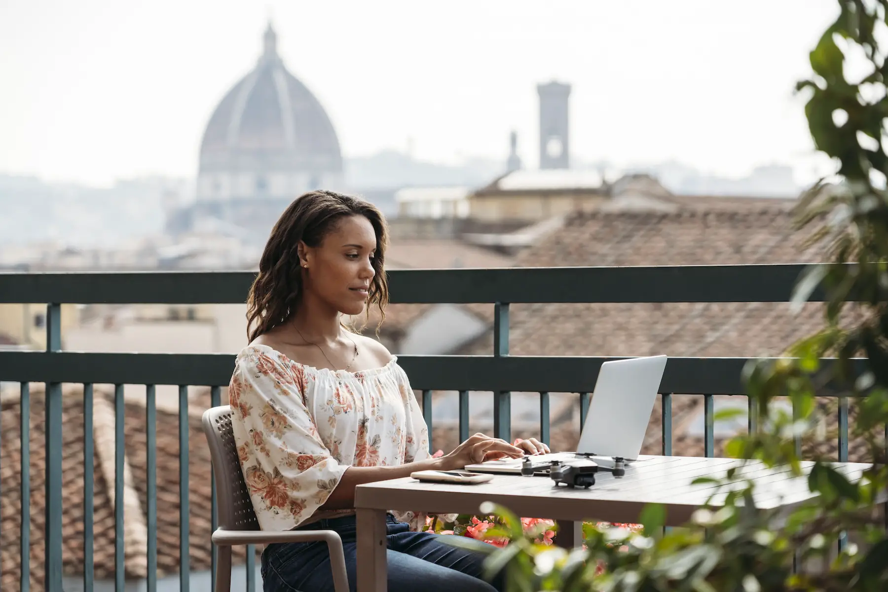 A woman sits using her laptop at a table on a balcony overlooking the city of Florence