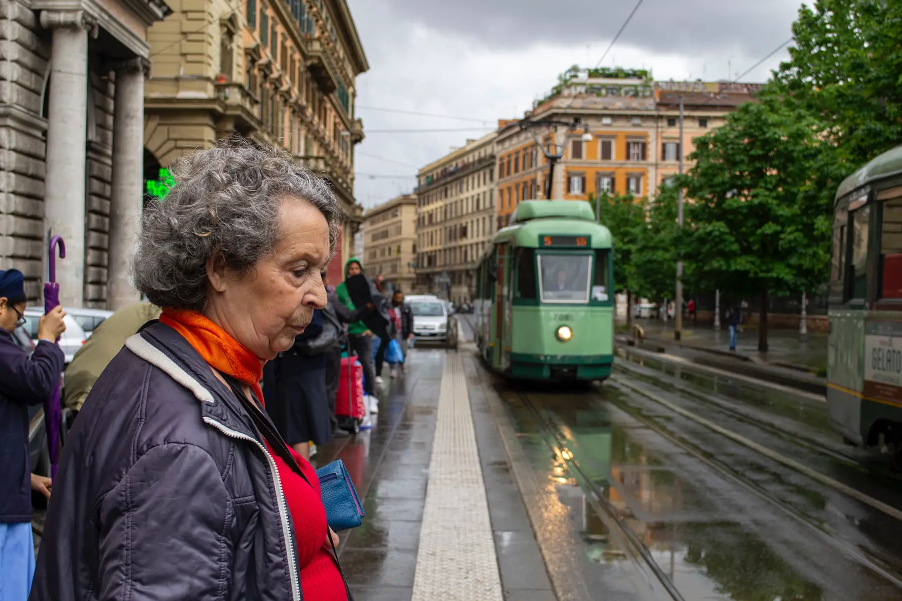 A woman waiting for an old-fashioned green tram on a rainy day.