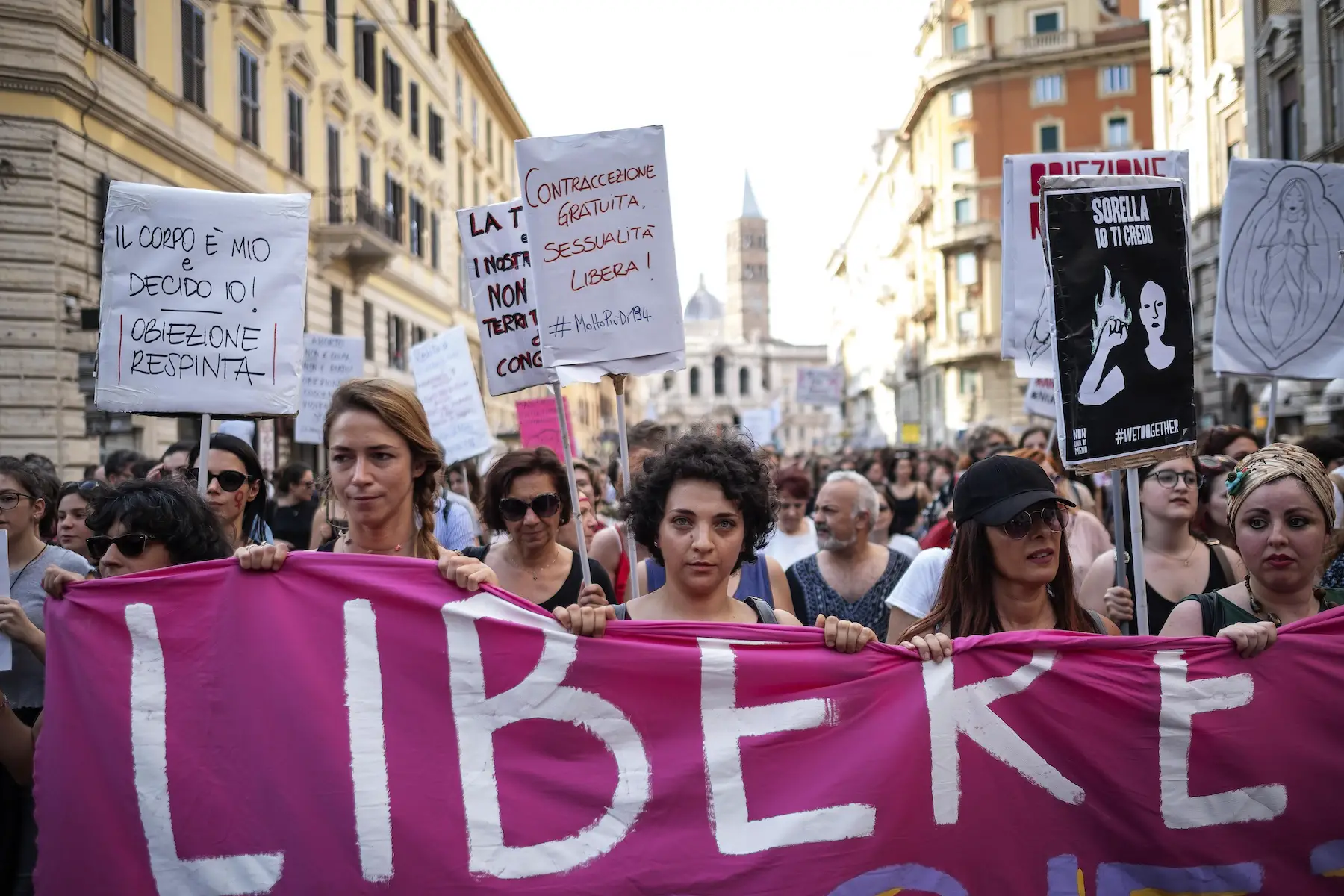 A large crowd of mostly women carries a pink banner and picket signs down the streets of Rome in support of abortion rights