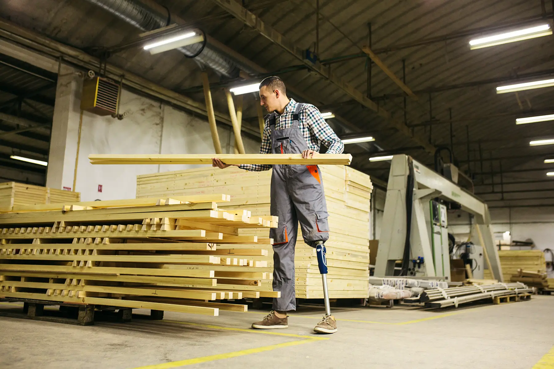 Carpenter with prosthetic leg choosing a plank from pile in warehouse