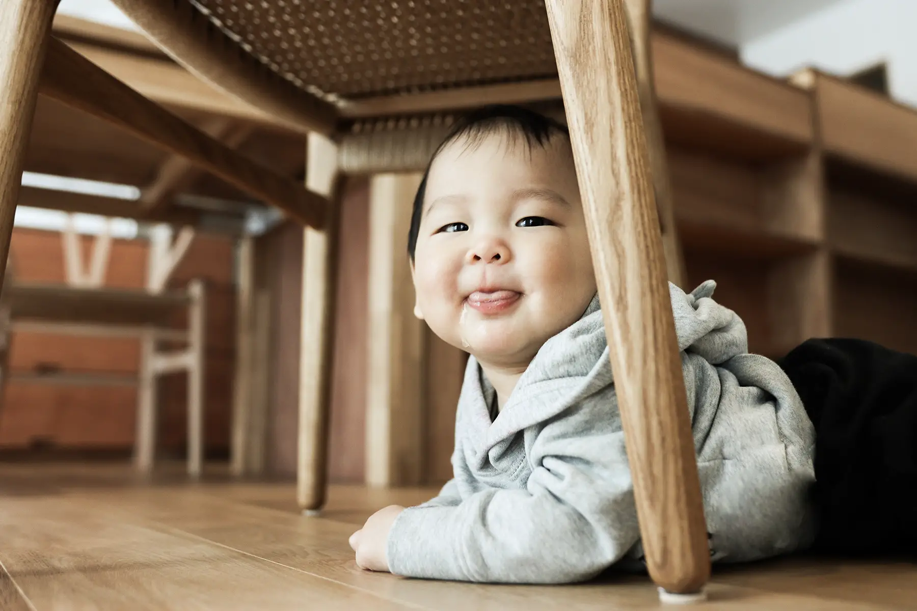 Cheeky little baby on their tummy underneath a table or chair - looking at camera