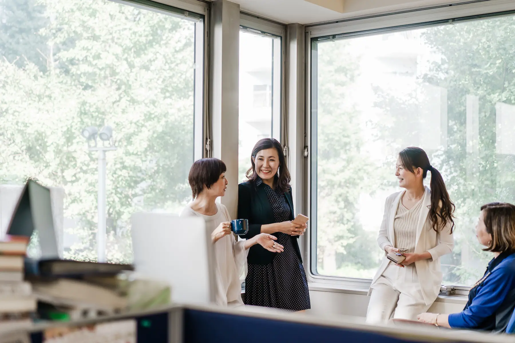 A group of relaxed businesswomen have a casual discussion in the office in front of windows