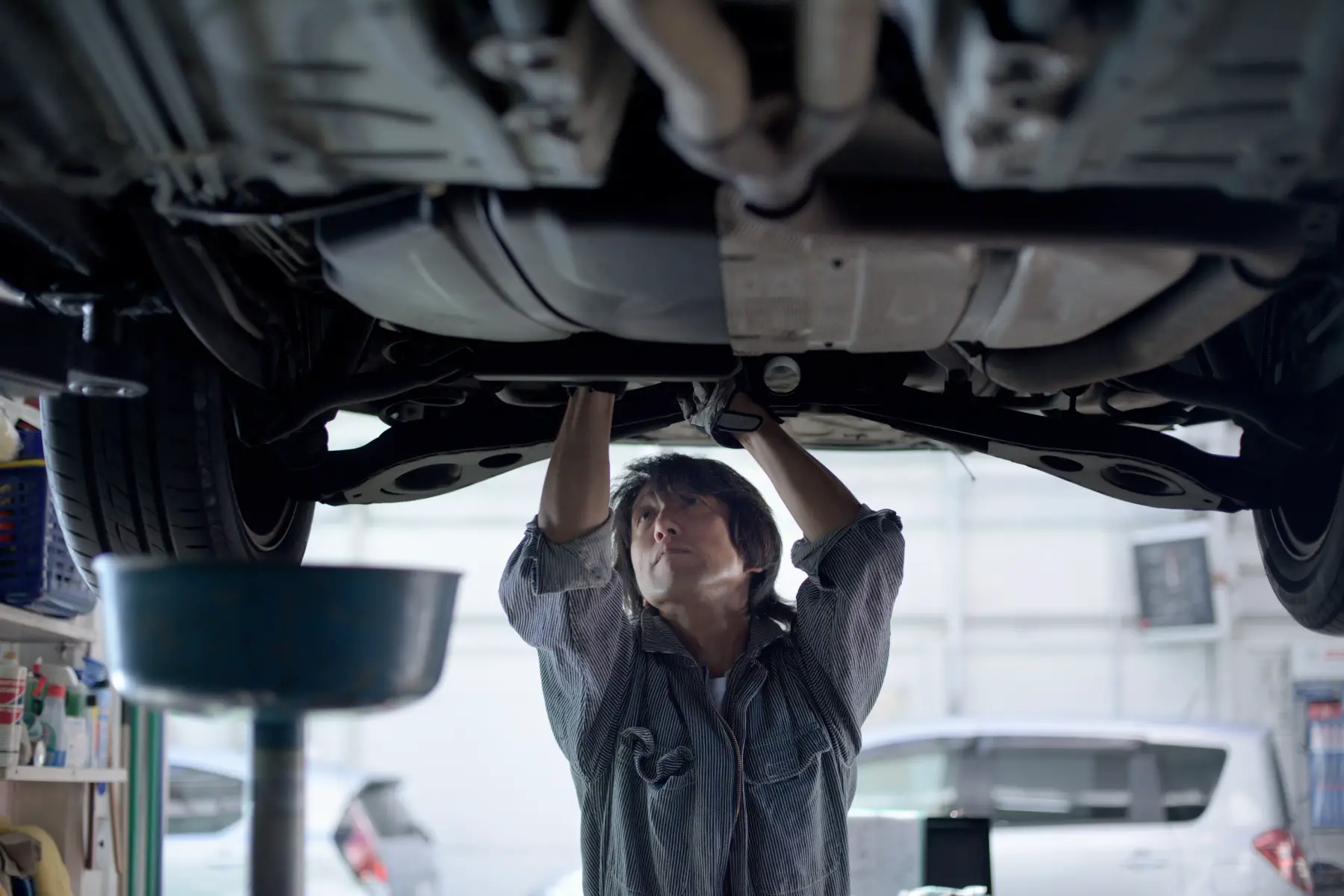 a mechanic repairing the underside of a car which hangs suspended above him 