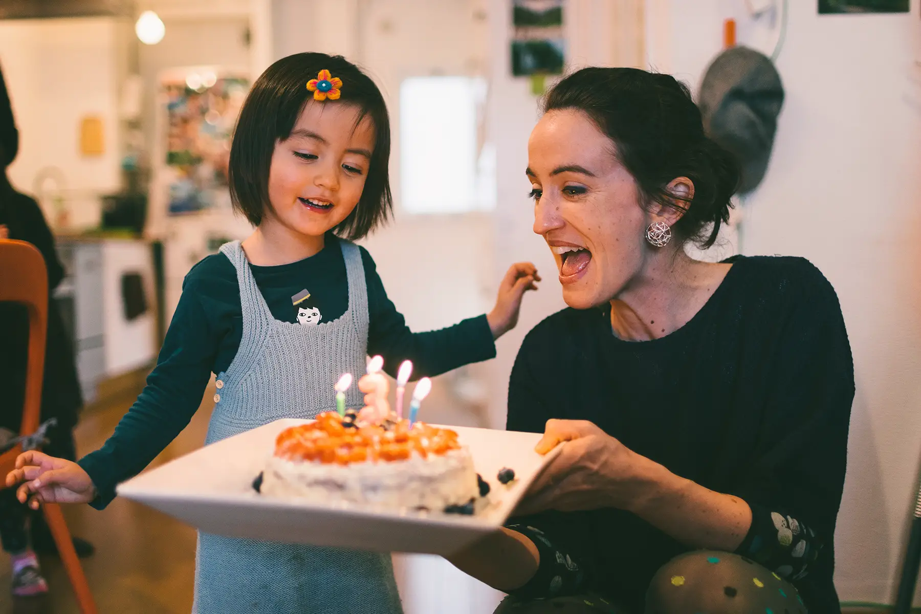 A child blowing out candles on a cake while an adult holds the cake up for them