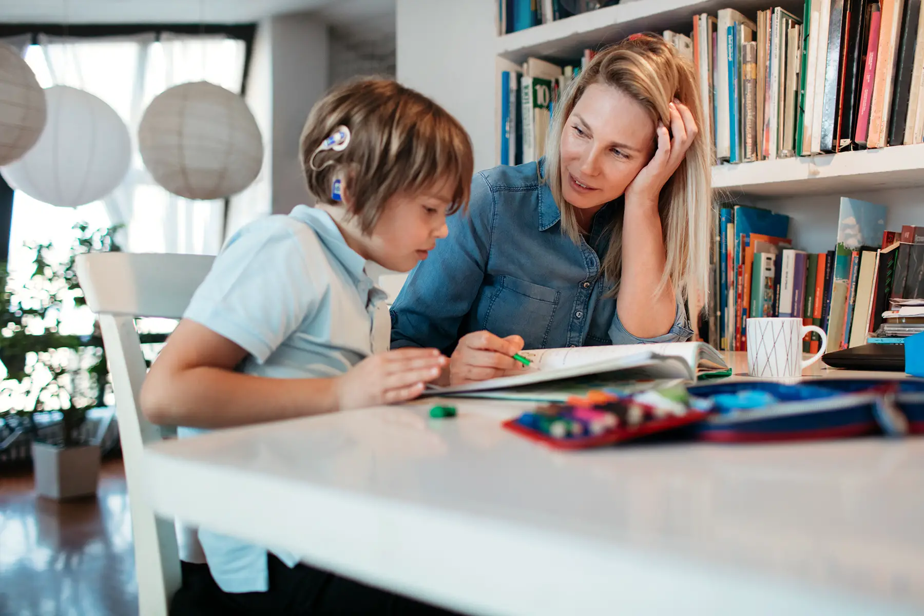 Mother and child with a cochlear implant looks at his homework or school applications